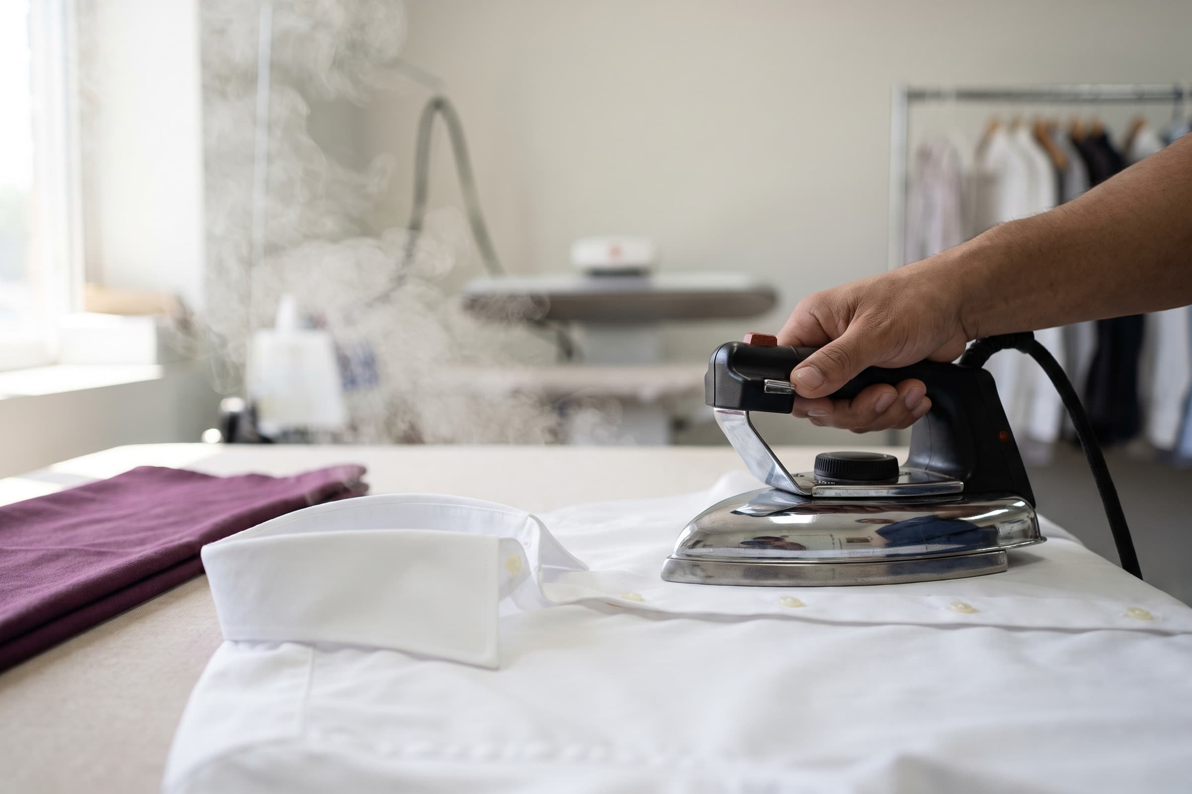 A chrome iron pressing a white dress shirt on a padded press table.