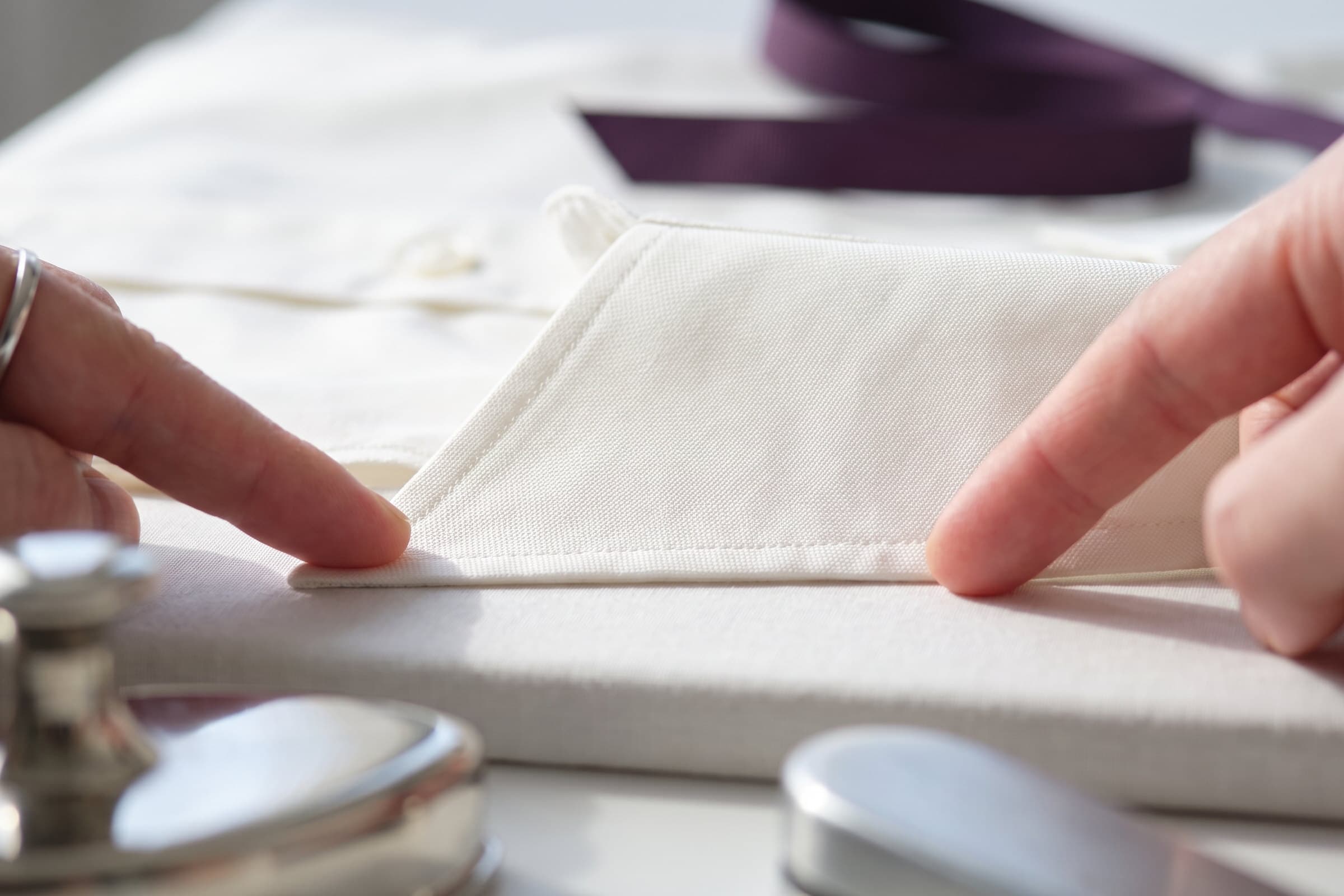 Close-up of two hands checking the stitched edge of a cream shirt on a padded press surface.
