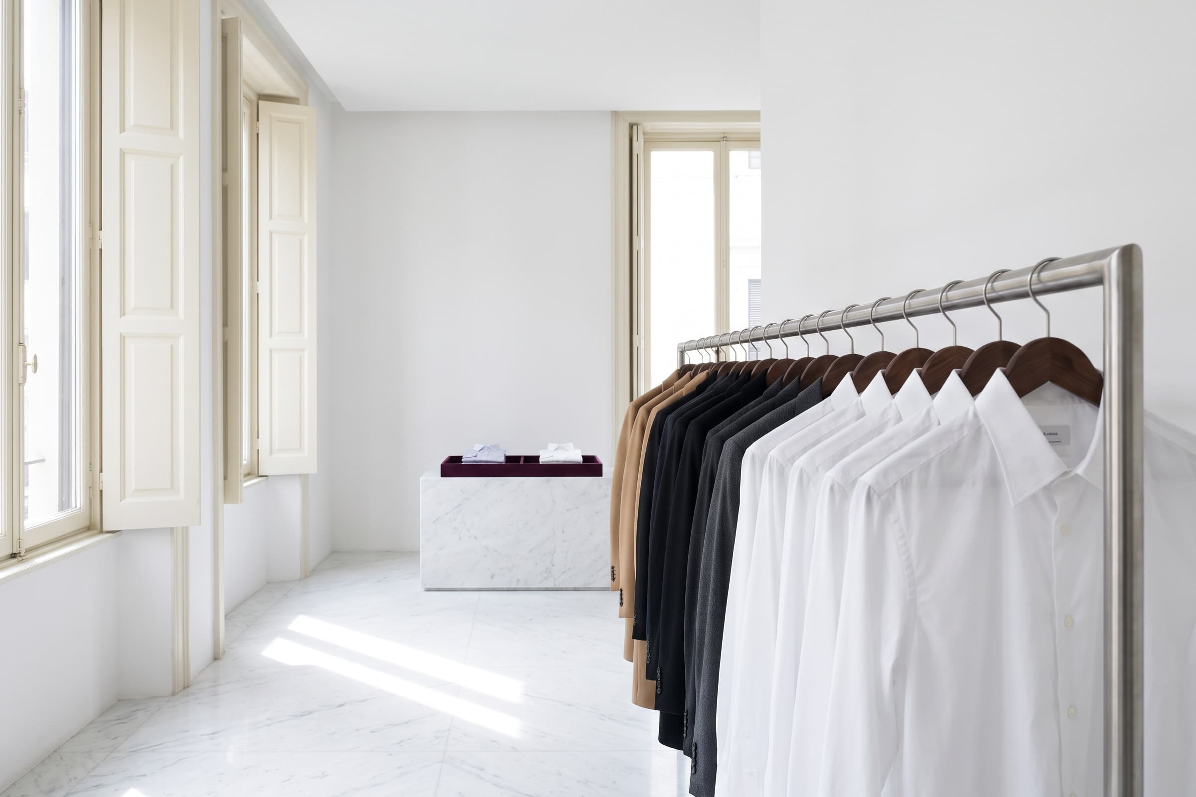 Freshly cleaned shirts and jackets on wooden hangers along a rail in a bright white room.