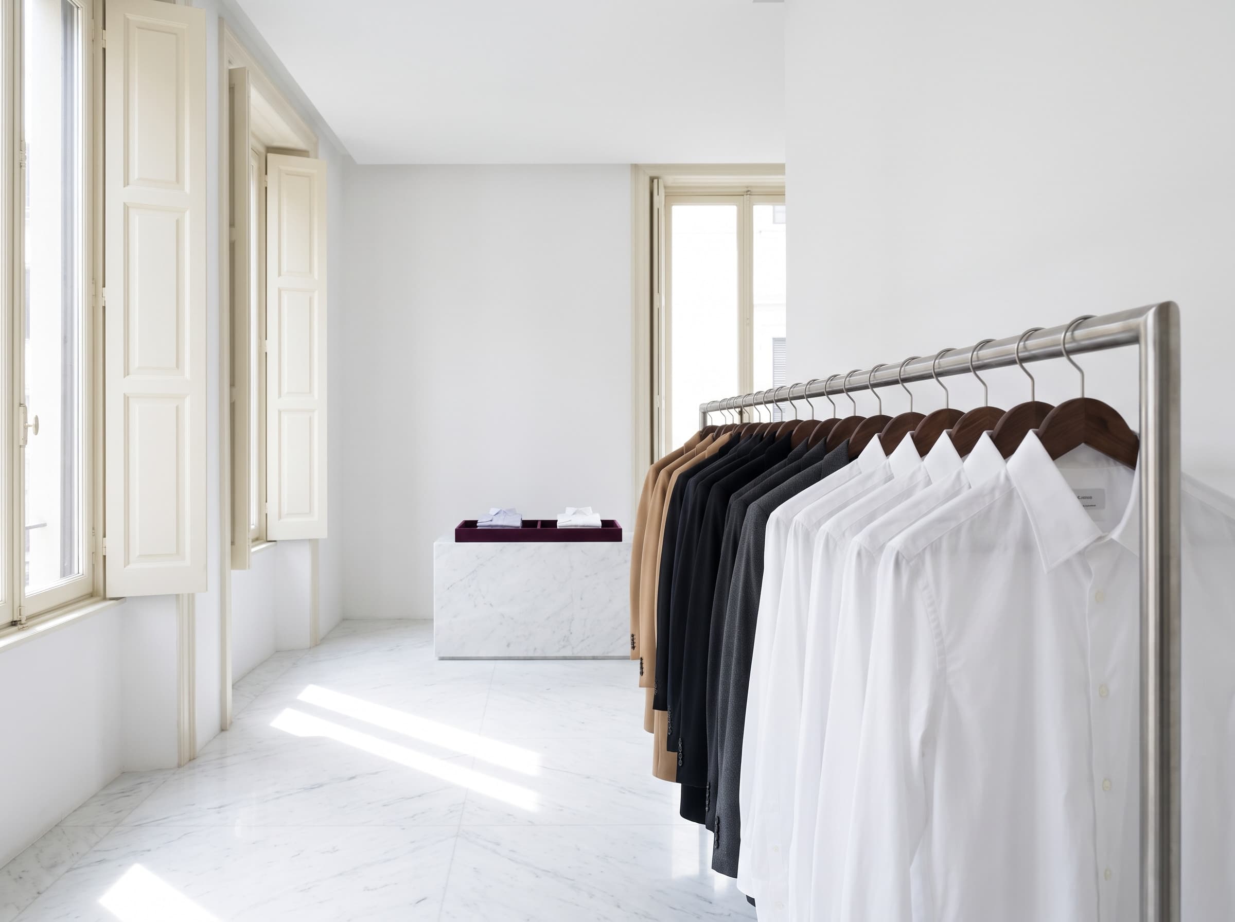 Freshly cleaned shirts and jackets on wooden hangers along a rail in a bright white room.