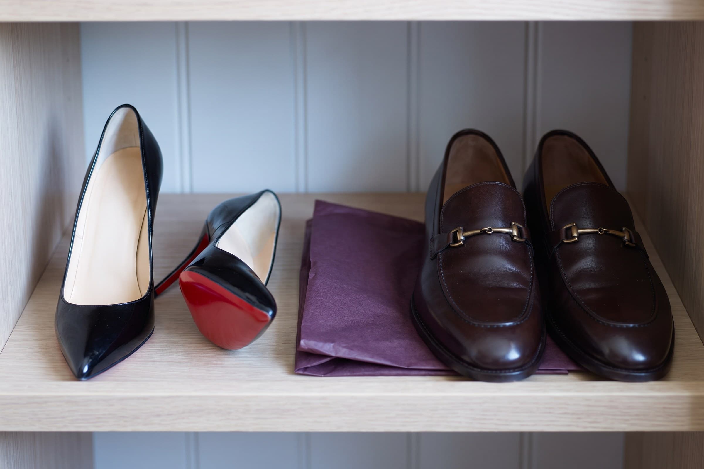 A pair of polished black patent pumps with red lacquered soles beside plum tissue paper.